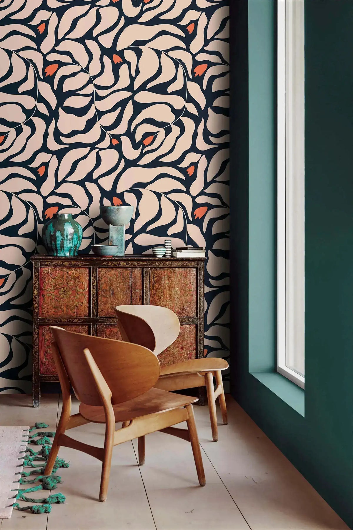 Botanical extravaganza wallpaper in corner; wooden lounge chair beside rustic cabinet with teal glazed vase and teal wall