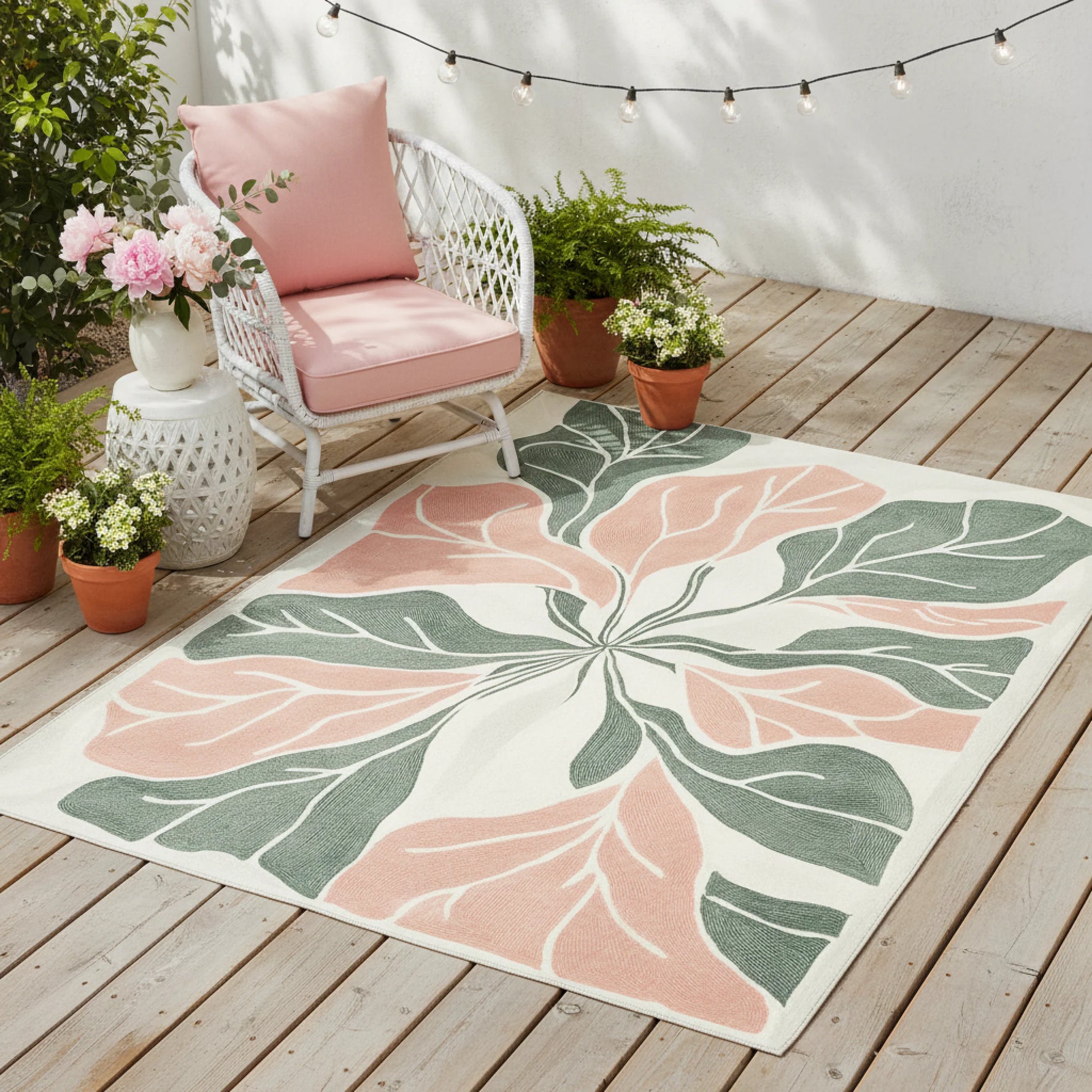 Decorative outdoor rug with leaf pattern on a wooden deck with plants and a chair.