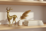 A decorative brass deer figurine stands on a light wood shelf beside a small white vase with dried pampas grass and a stack of white books against a warm beige wall.