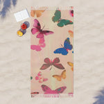 Pink beach towel multicolor butterfly print laid flat on sand aerial view with fruit and book