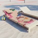 Butterfly Dreamscape Pink Beach Towel draped over white lounge chair on sandy beach with volleyball