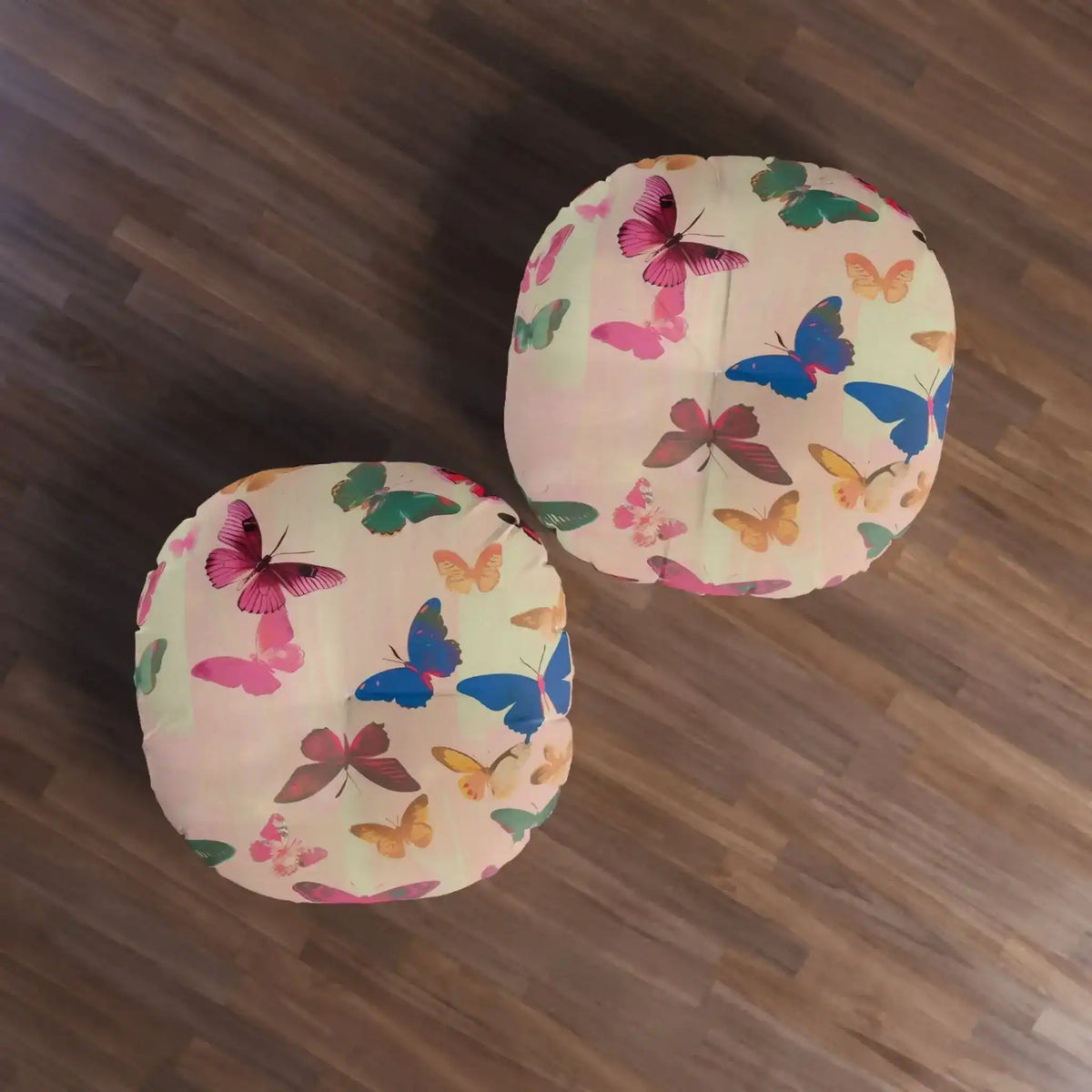 Two square Butterfly Kisses Dreamy Pink Flight Floor Pillows on hardwood floor overhead view with colorful butterfly pattern across blush fabric