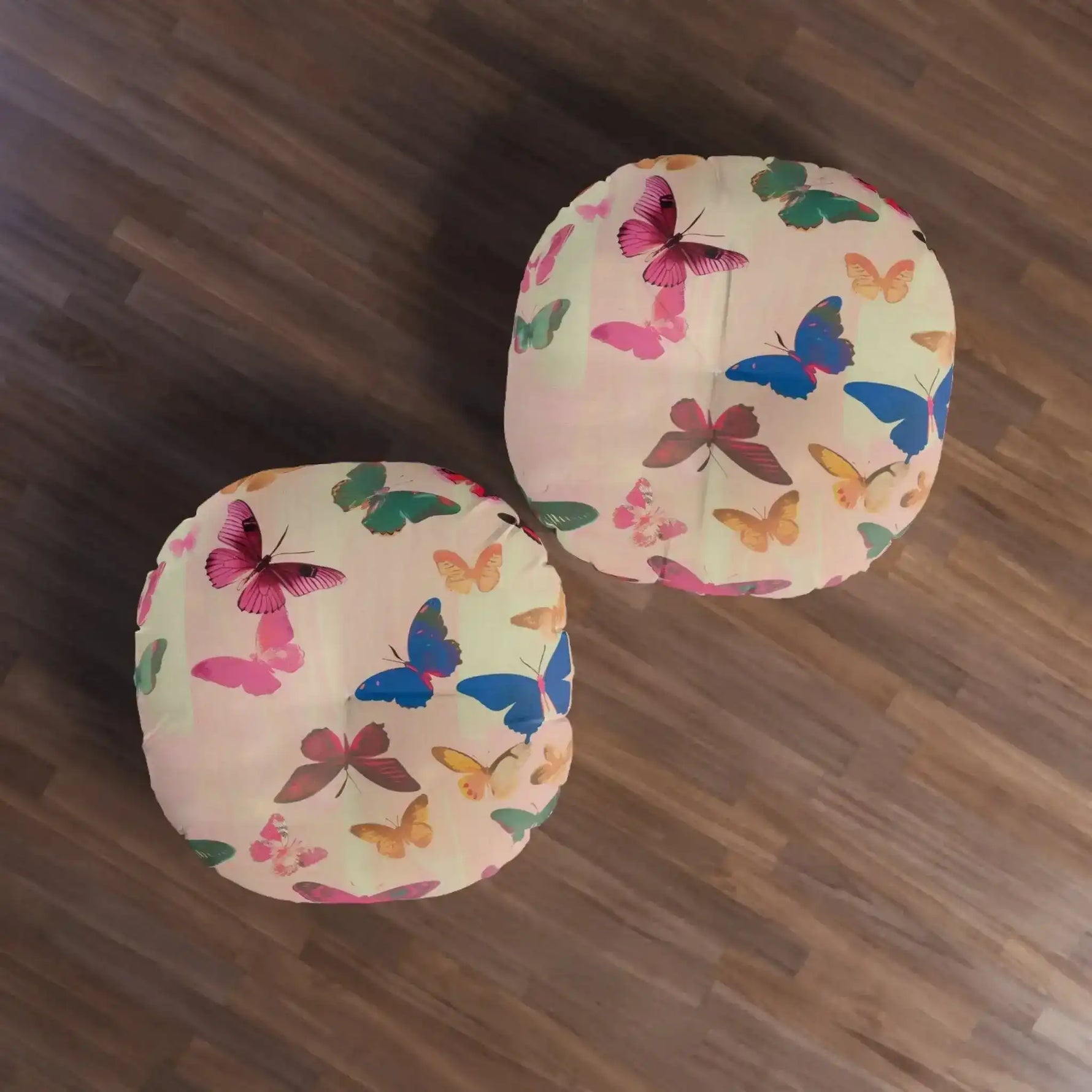 Two square Butterfly Kisses Dreamy Pink Flight Floor Pillows on hardwood floor overhead view with colorful butterfly pattern across blush fabric