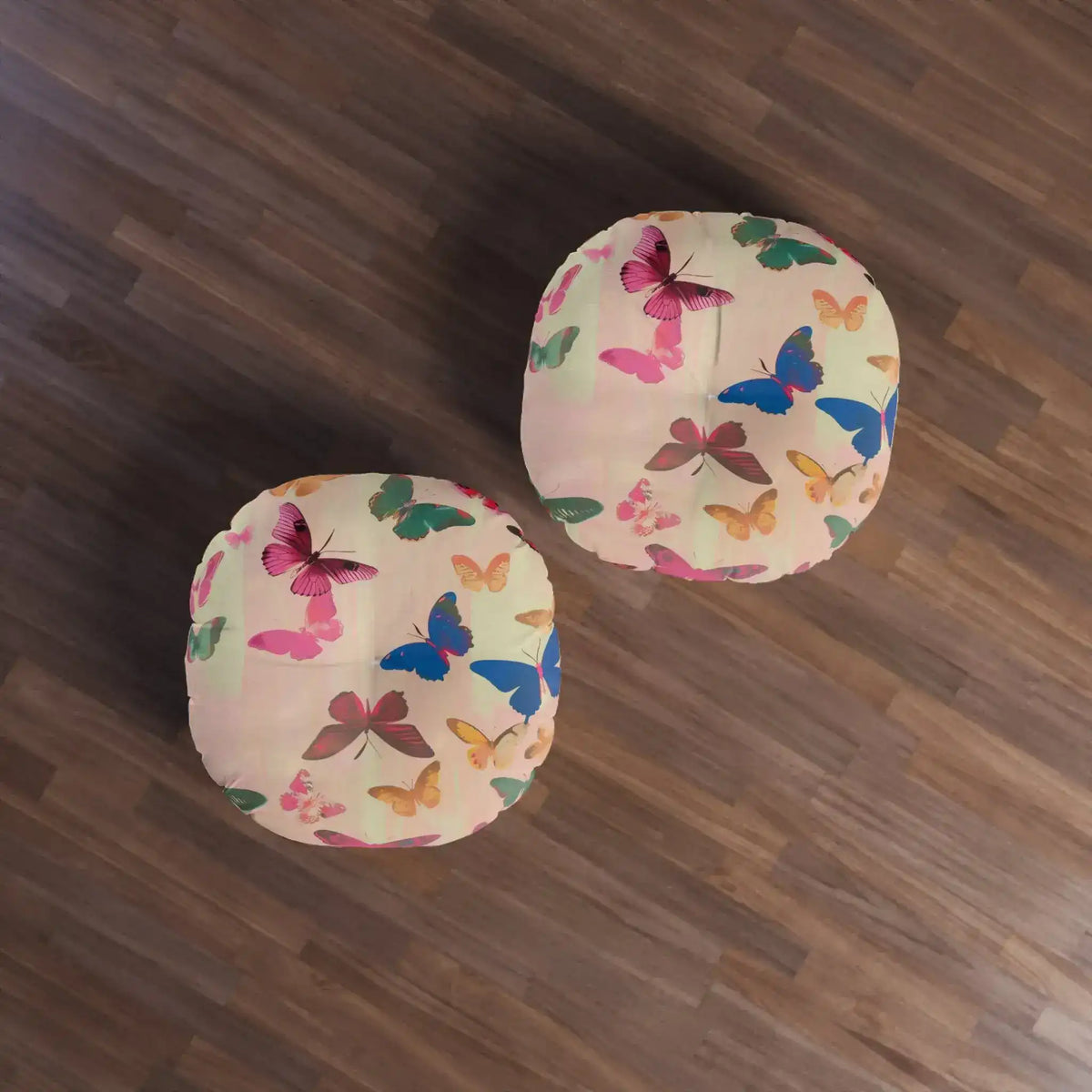 Two Butterfly Kisses Dreamy Pink Flight Floor Pillows placed on dark wood floor from a top-down view showing colorful butterfly print fabric