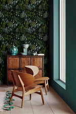 Carved cabinet and wooden chairs against enigmatic leafy canopy wallpaper, deep green foliage