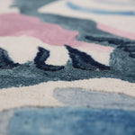 Close-up of a textured rug with geometric patterns in blue, pink, and white.