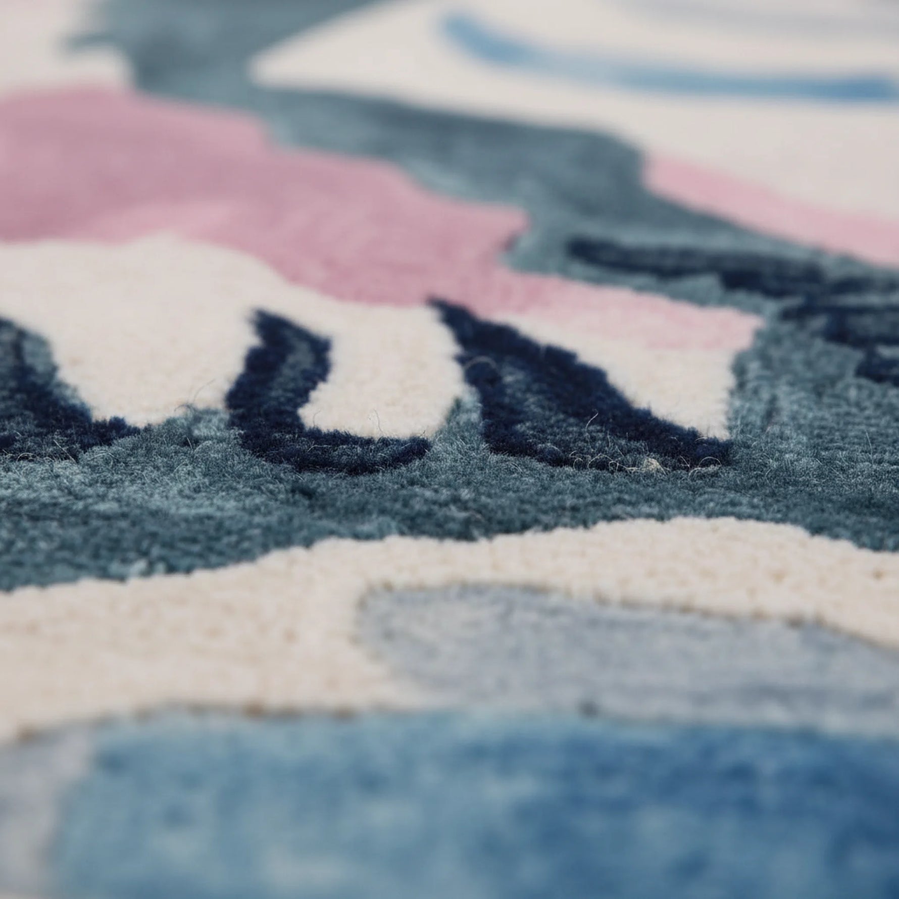 Close-up of a textured rug with geometric patterns in blue, pink, and white.