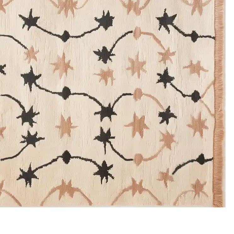 Top view of the Celestial Rhapsody Knotted Wool Rug, featuring a striking abstract star pattern in black and beige on a cream background. This area rug adds a touch of elegance and modern design to any space.