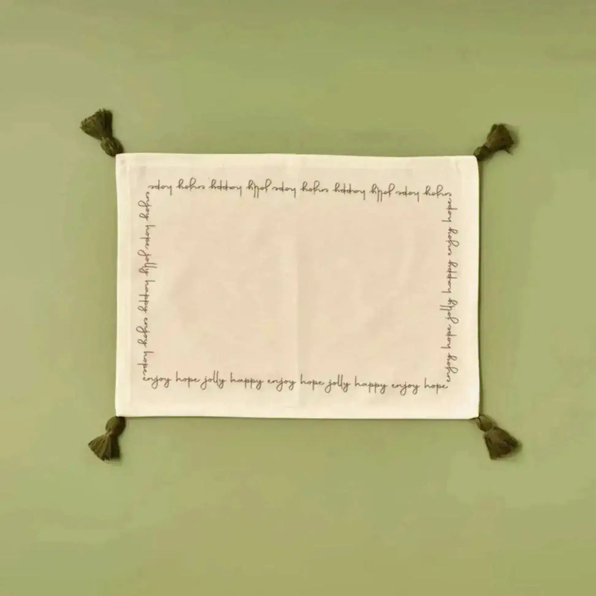 Cheerful Corner Placemats white linen with festive script border and olive corner tassels, flat lay on sage green