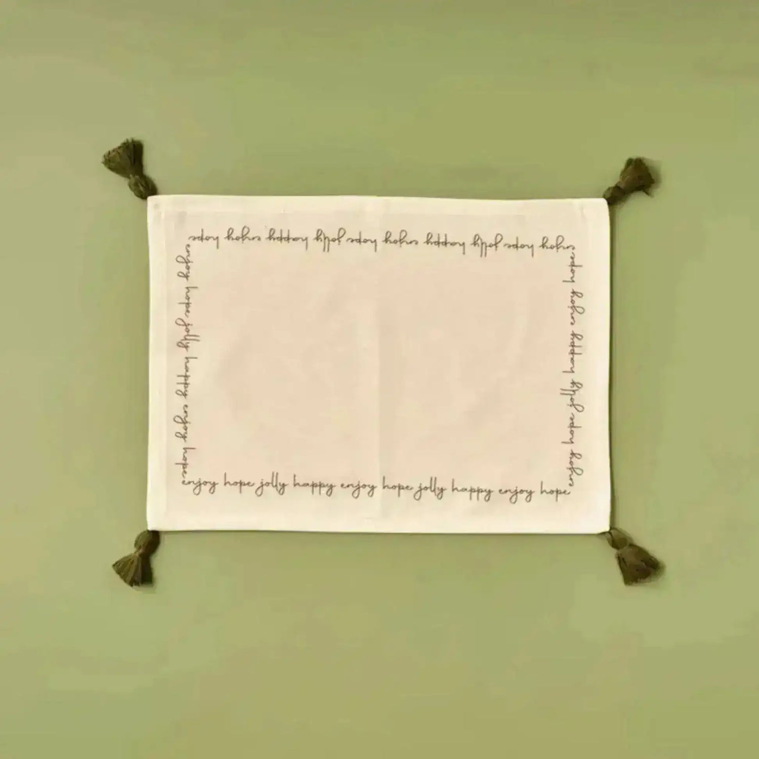 Cheerful Corner Placemats white linen with festive script border and olive corner tassels, flat lay on sage green