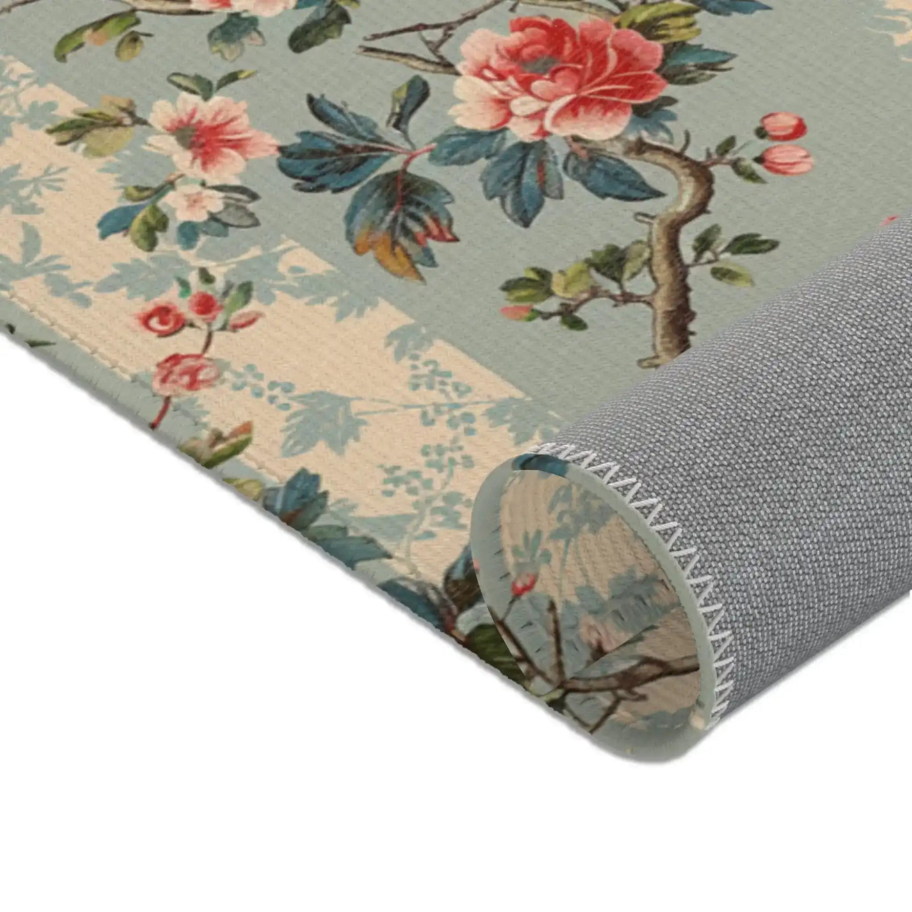 Chinoiserie charm rug corner rolled up, bold pink rose bloom and leaves above gray fabric backing