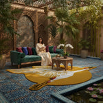 Woman sitting on a green couch in a decorative indoor setting with plants and a colorful rug.