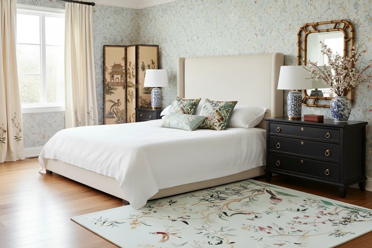 Neatly made bed in a bedroom with a chinoiserie chic rug, and decorative elements.