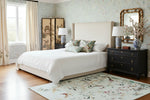 Neatly made bed in a bedroom with a chinoiserie chic rug, and decorative elements.