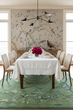 Dining room with a table set for a meal, floral centerpiece, and decorative wall and  green knotted rug.