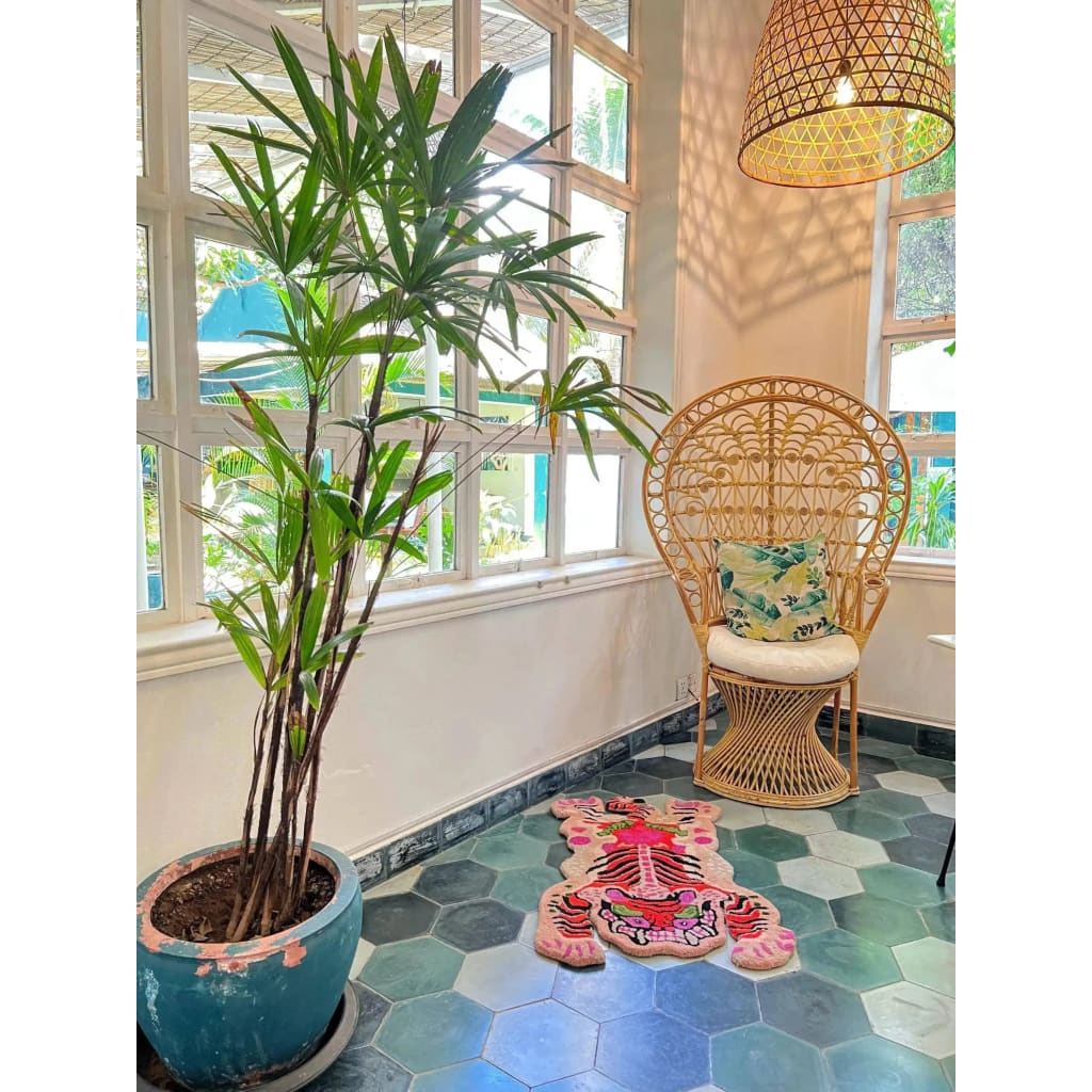 A stylish living room features a Chinoiserie Pink Tibetan Tiger Tufted Wool Rug on a hexagonal tile floor. The area rug adds a vibrant touch with its abstract tiger design, complementing the rattan chair and lush green plant, perfect for enhancing large living room spaces with a touch of elegance.