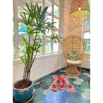 A stylish living room features a Chinoiserie Pink Tibetan Tiger Tufted Wool Rug on a hexagonal tile floor. The area rug adds a vibrant touch with its abstract tiger design, complementing the rattan chair and lush green plant, perfect for enhancing large living room spaces with a touch of elegance.