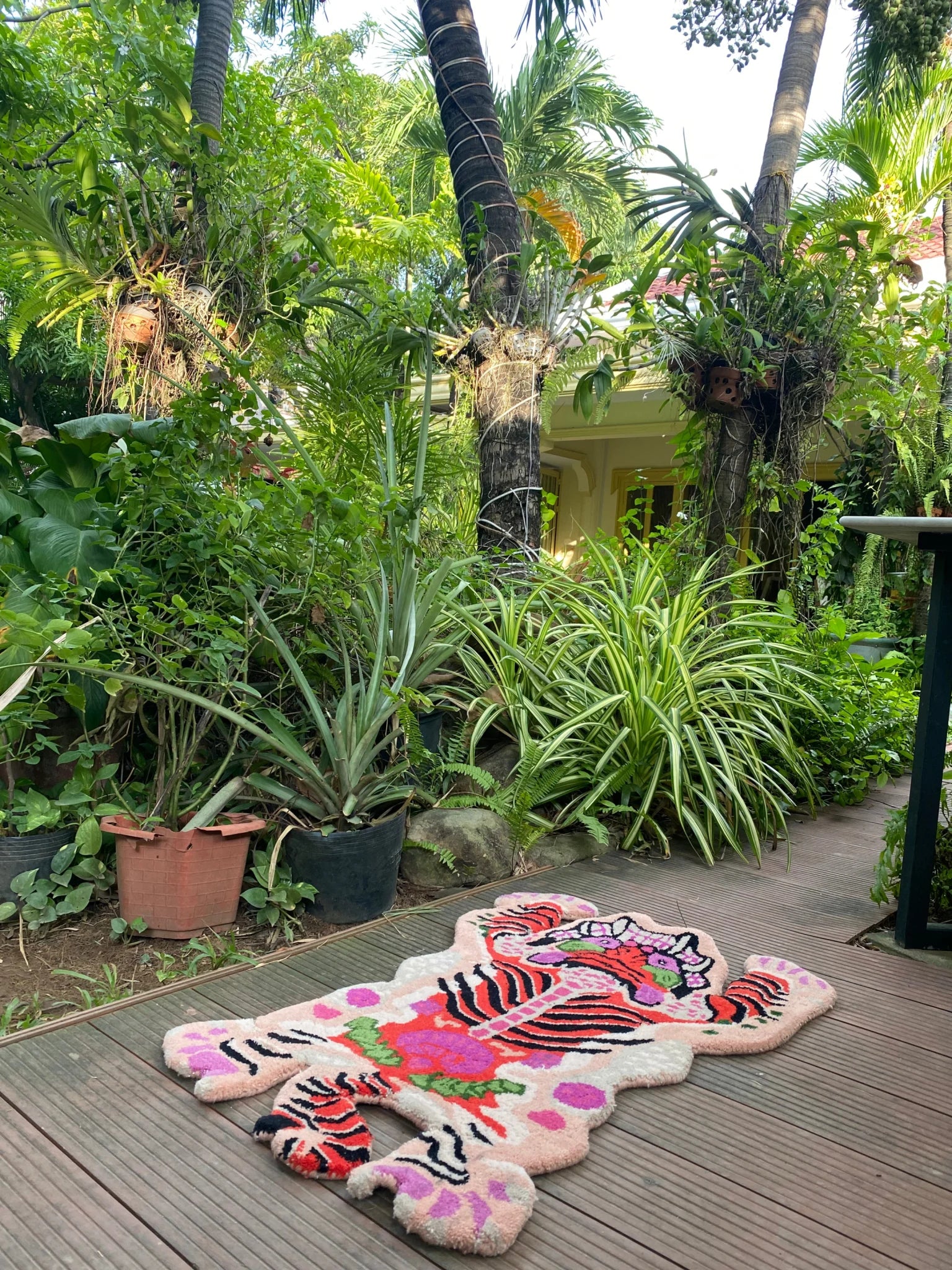 This vibrant Chinoiserie Tibetan Tiger hand-tufted wool rug in pink showcases an abstract tiger design, perfect for adding a touch of exotic flair to living rooms and dining rooms. The area rug is displayed outdoors on a wooden deck surrounded by lush greenery, highlighting its suitability as a large living room rug or for use in a dining room setting.