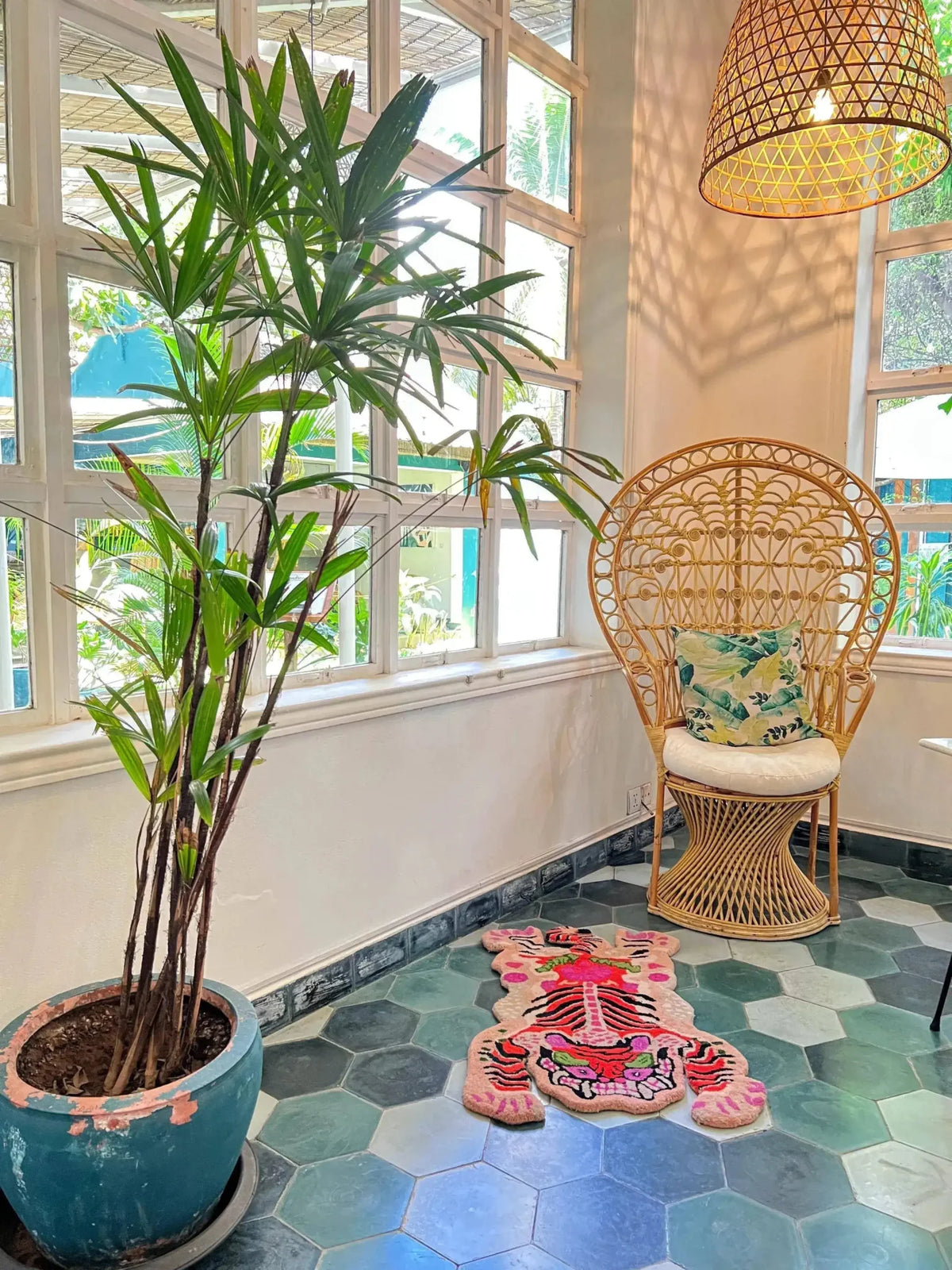 Bright and vibrant Chinoiserie Tibetan Tiger hand-tufted wool rug in pink, adding a touch of exotic flair to a cozy corner of a living room. The area rug is laid over hexagonal tiles, complementing the wicker chair and lush indoor plant, perfect for large living room and dining room spaces.