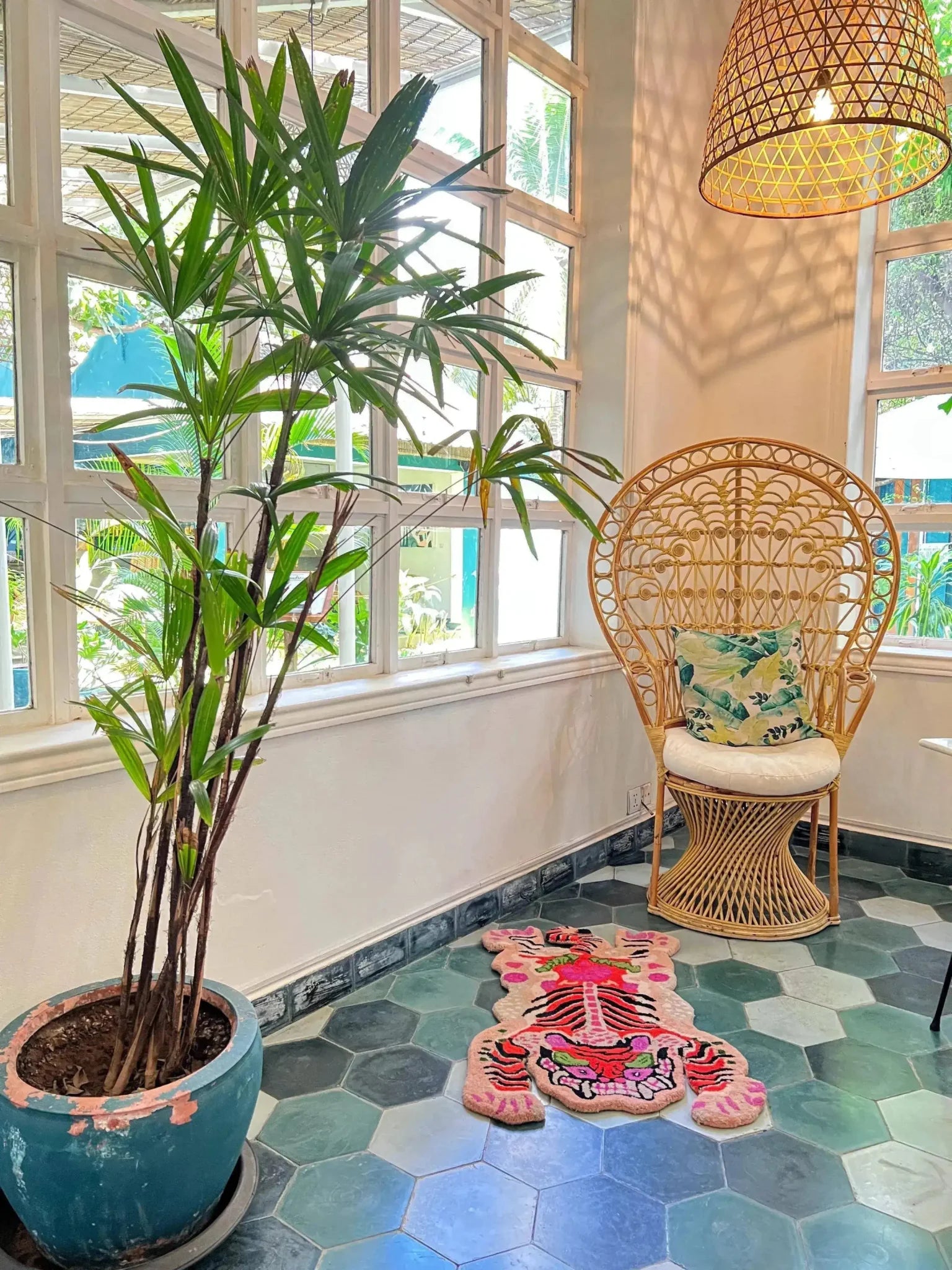 Bright and vibrant Chinoiserie Tibetan Tiger hand-tufted wool rug in pink, adding a touch of exotic flair to a cozy corner of a living room. The area rug is laid over hexagonal tiles, complementing the wicker chair and lush indoor plant, perfect for large living room and dining room spaces.
