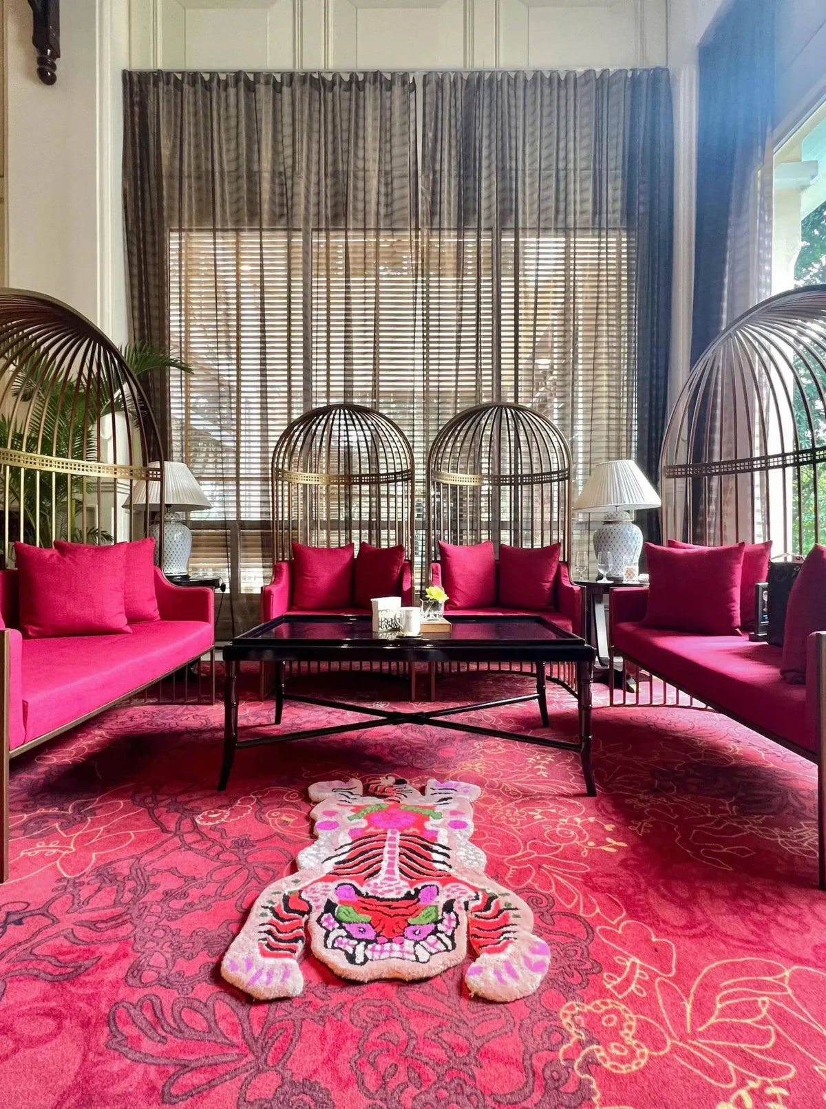 This vibrant living room showcases a Chinoiserie Tibetan Tiger Hand Tufted Wool Rug in pink, adding a bold and artistic flair to the space. Perfect for both living room and dining room settings, this large area rug features an abstract tiger design that stands out against the elegant decor. The wool rug complements the rich red seating and creates a cohesive look in this stylish, well-lit room.