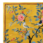 A vibrant corner detail of the Chirping Cherry Tree Hand Tufted Area Rug, showcasing a rich yellow background with intricate patterns of blooming flowers and perched birds, exuding a lively and artistic touch.
