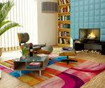 A vibrant Chroma Groove Hand Tufted Area Rug in a cozy living room setting. The large wool rug features bold, colorful abstract patterns, enhancing the modern decor with a fireplace, bookshelves, and comfortable seating. Perfect for living room and dining room rugs, this stylish piece adds warmth and character.