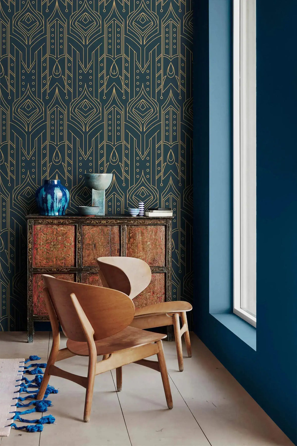 Cityscape glam wallpaper with gold line Art Deco motifs on navy, paired with a carved cabinet, blue vase, wood lounge chair