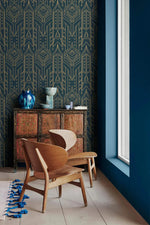 Cityscape glam wallpaper with gold line Art Deco motifs on navy, paired with a carved cabinet, blue vase, wood lounge chair