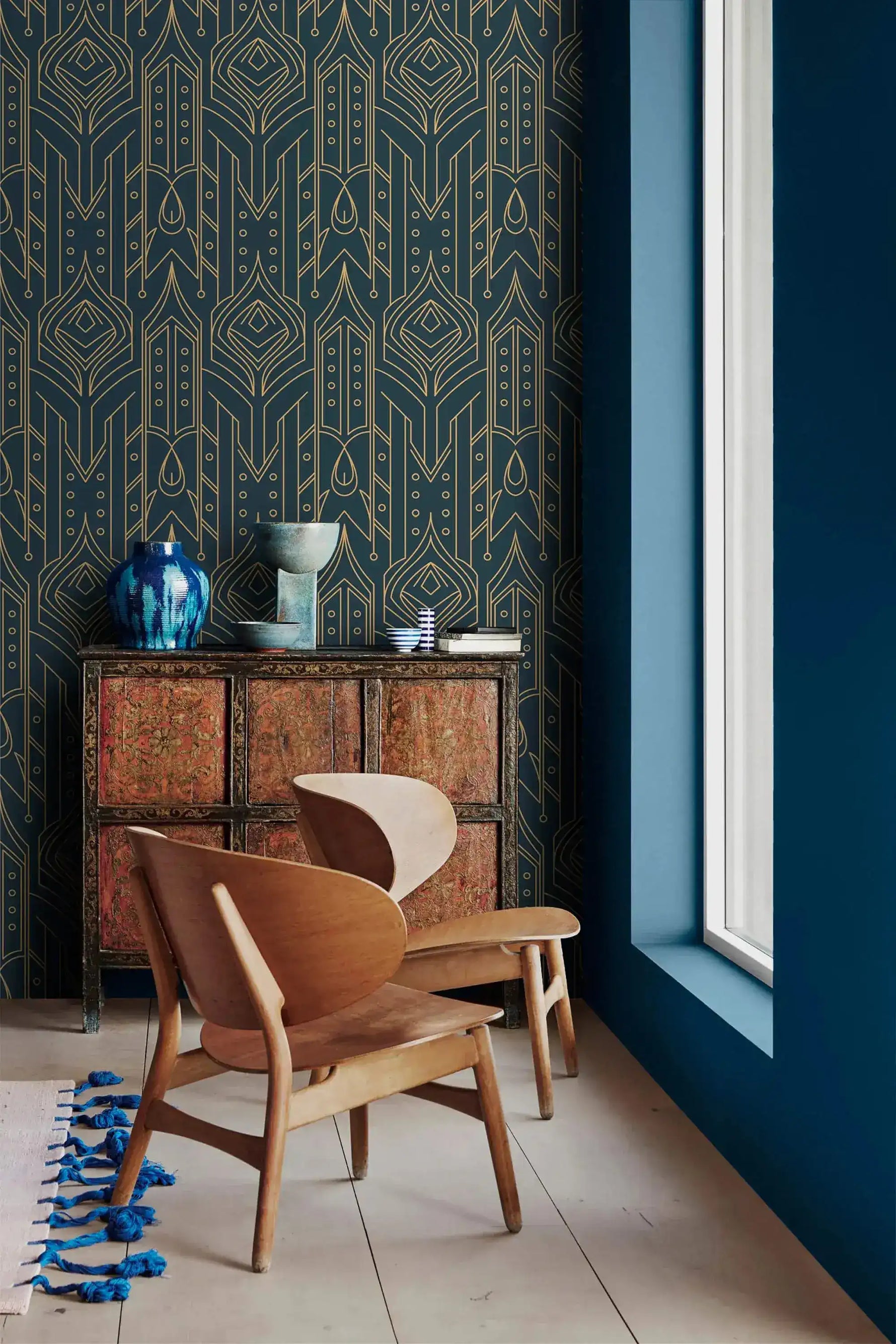 Cityscape glam wallpaper with gold line Art Deco motifs on navy, paired with a carved cabinet, blue vase, wood lounge chair