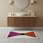 Bathroom with wooden vanity, round mirror, and colorful bow-shaped rug on floor.