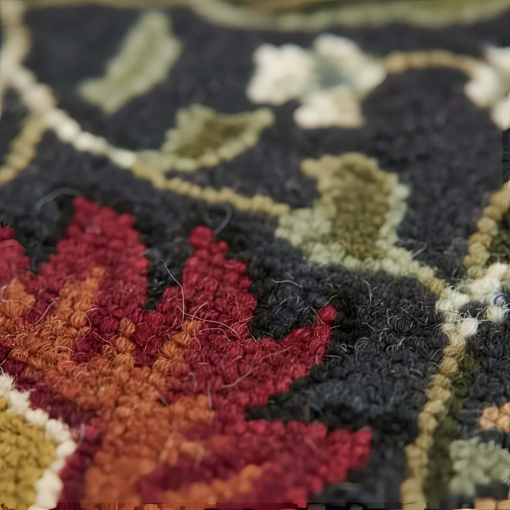 Close-up of a textured rug with autumn leaf pattern in red, orange, and green on a dark background.