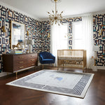 Nursery room with geometric wallpaper, blue chair, wooden crib, and decorative rug.