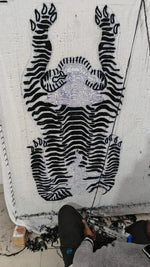 Artisan crafting a Classic Tiger Yogi Accent Wool Rug, showcasing an intricate black and white tiger design. Perfect for adding a unique touch to your office or bedroom with a stylish area rug.