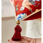 Close-up of a red chinoiserie inspired throw pillow cover featuring intricate patterns and decorative tassels.