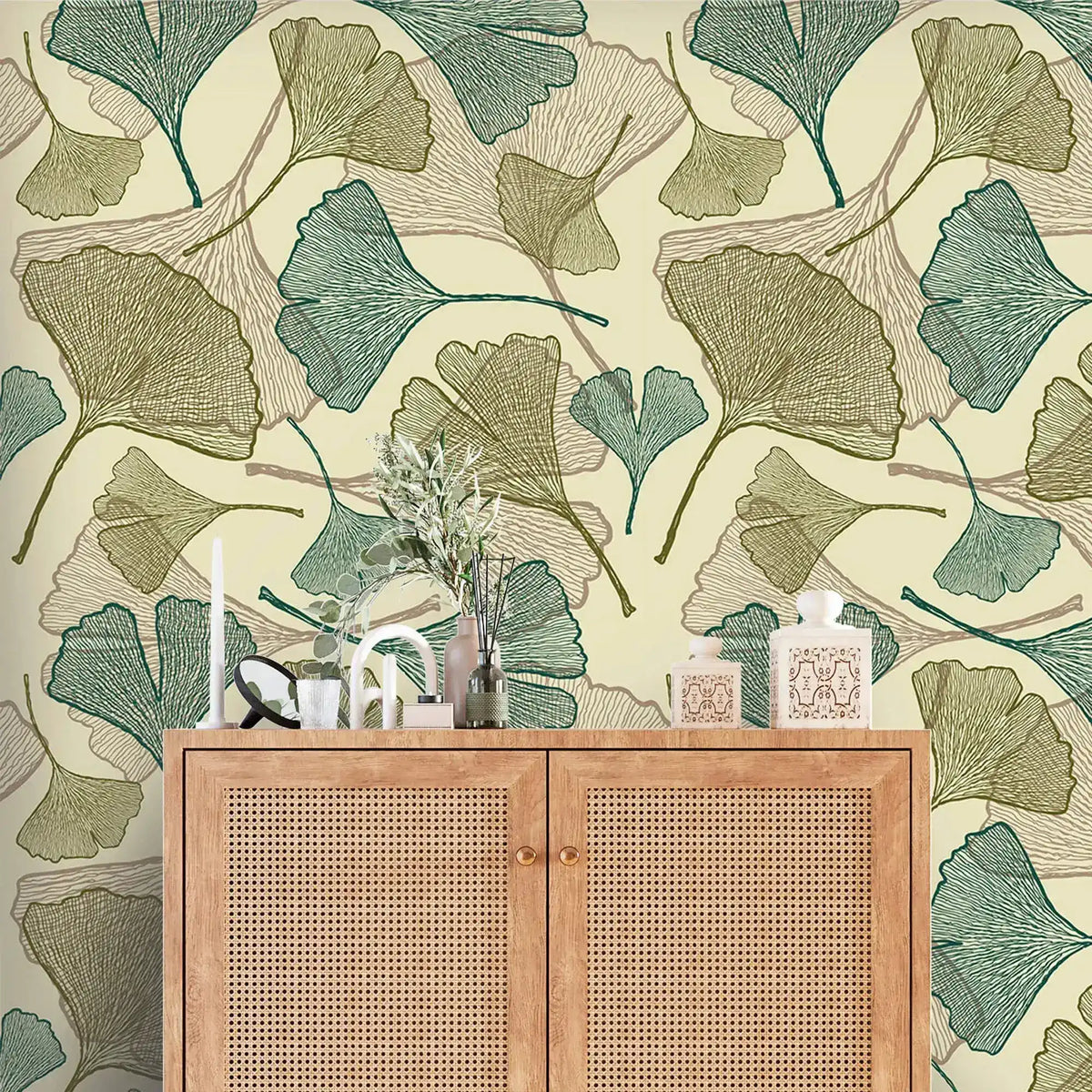 Close-up of green and olive ginkgo leaf wallpaper behind cane rattan cabinet with vases