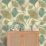 Close-up of green and olive ginkgo leaf wallpaper behind cane rattan cabinet with vases