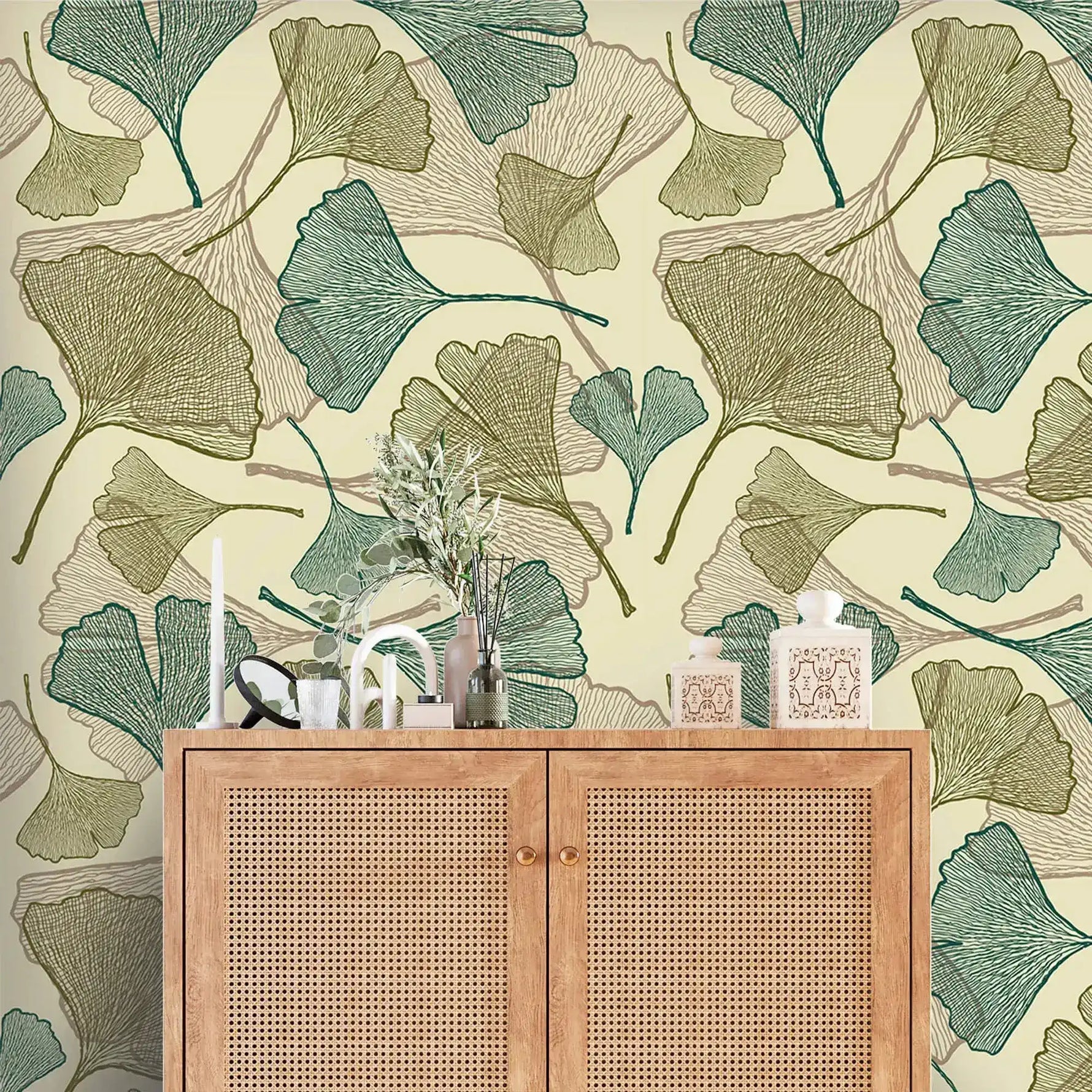 Close-up of green and olive ginkgo leaf wallpaper behind cane rattan cabinet with vases