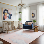 Modern nursery with a crib, pink cloud rug, blue armchair, and abstract art on the walls.