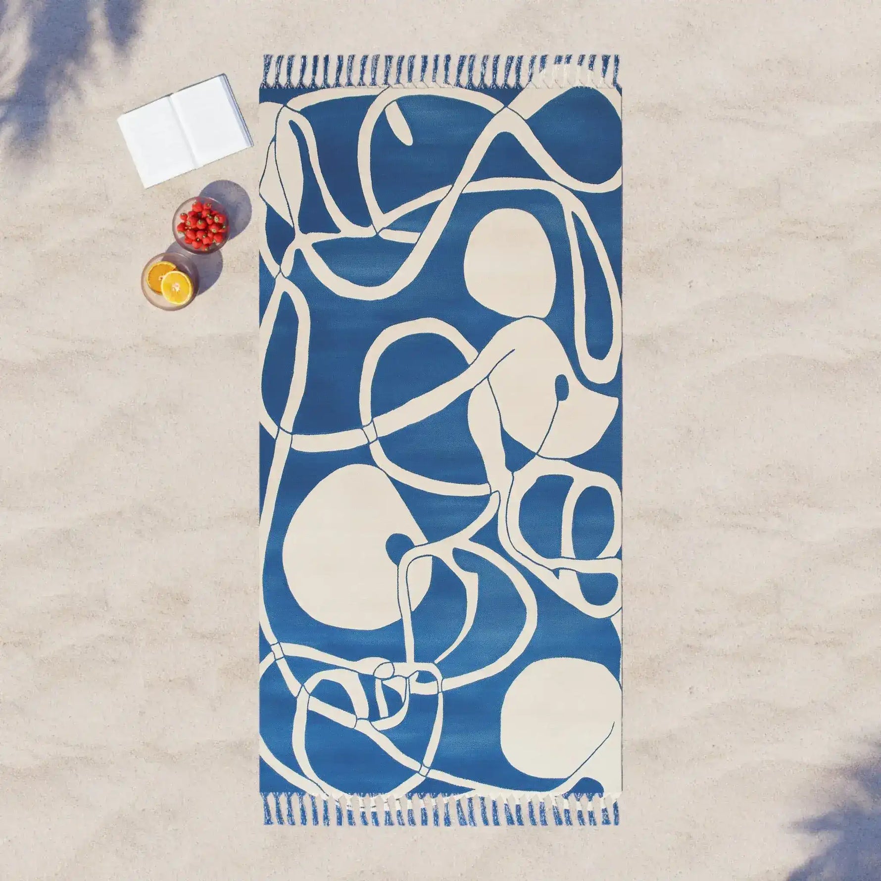 Coastal Waves Abstract Blue and White Beach Towel flat on sand from above with open book and fruit bowl beside