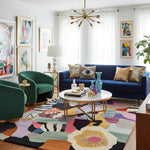 Modern living room with a blue sofa, green armchairs, and colorful rug.