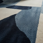 A stylish hand tufted area rug with an abstract design in shades of blue and white. This contemporary wool rug is perfect for adding a modern touch to any living room, showcasing a unique pattern that complements various decor styles.