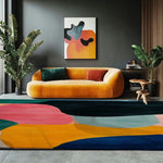 A vibrant and large area rug with abstract design featuring bold colors like pink, yellow, and blue, perfectly complementing a modern living room setup. The wool rug adds a touch of elegance and warmth to the space, with a cozy orange sofa and artistic wall decor enhancing the room's contemporary vibe.