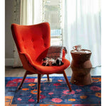 A vibrant and colorful hand-tufted wool area rug, perfect for adding warmth to your living room or dining room. The rug features an abstract floral design in rich blues and oranges, complementing the cozy orange chair and wooden side table in this stylish setting.