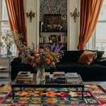 Colorful Tibetan blossom rug under a glass table by a dark velvet sofa in an eclectic room