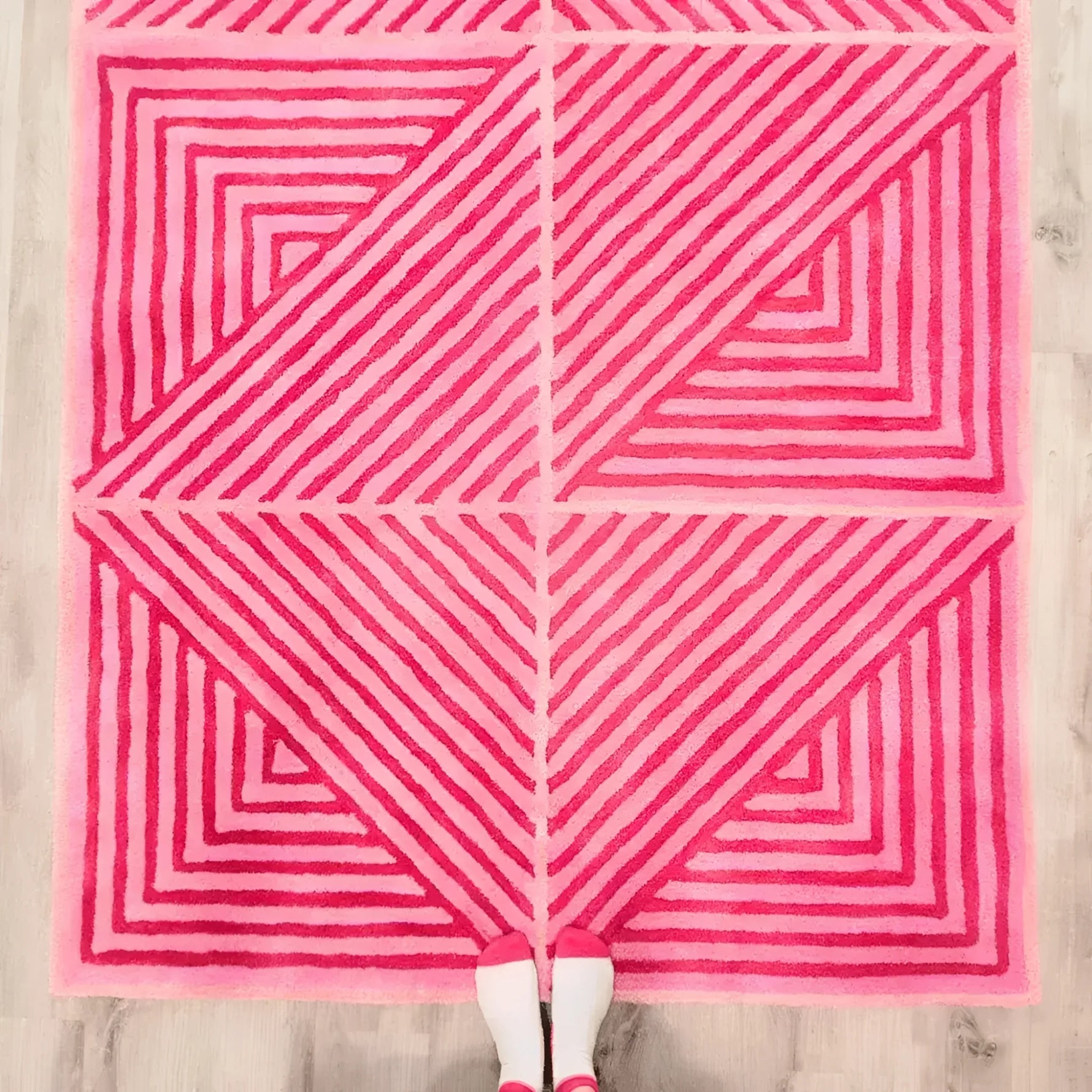 Top view of a contemporary hot pink geometric wool area rug, featuring bold triangular patterns with varying shades of pink stripes. Perfect for large living room rugs or dining room carpets, adding a vibrant touch to any dining room or living room space.