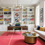 Modern living room with bookshelves, a desk, and colorful rug.