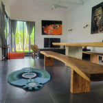 Contemporary round evil eye hand tufted wool rug placed in a modern living room with large windows, wooden furniture, and artistic wall decor. The area rug's bold circular design adds a unique touch to the serene bedroom setting, perfect as a statement piece among large area rugs.