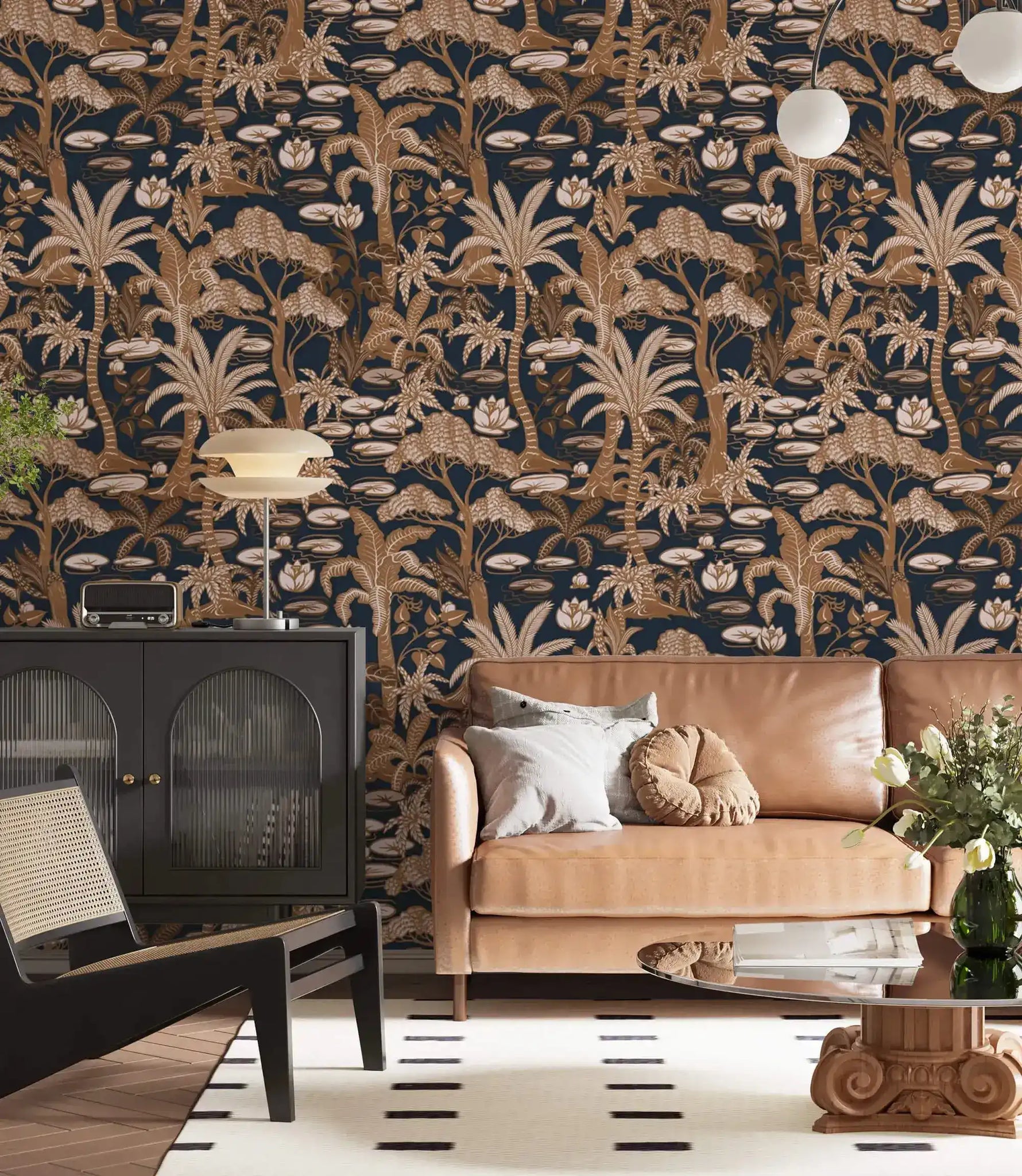 Copper palm tree wallpaper on navy in a living room with tan sofa, black cabinet and globe lamps