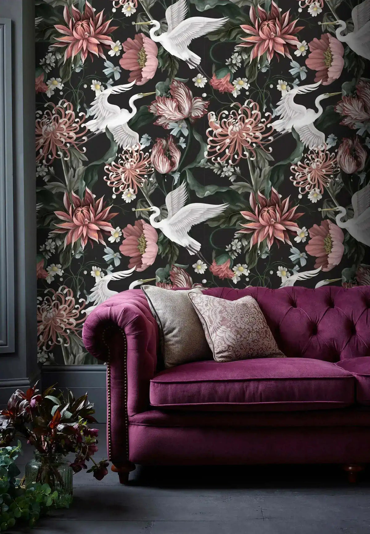 Dark moody room setting with purple Chesterfield sofa against crane and bloom wallpaper in deep botanical tones